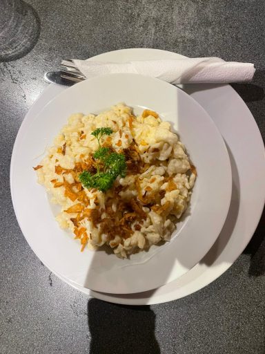 Käßspätzle Eine Portion Risotto mit grüner Petersilie und Parmesan, serviert auf einem weißen Teller.